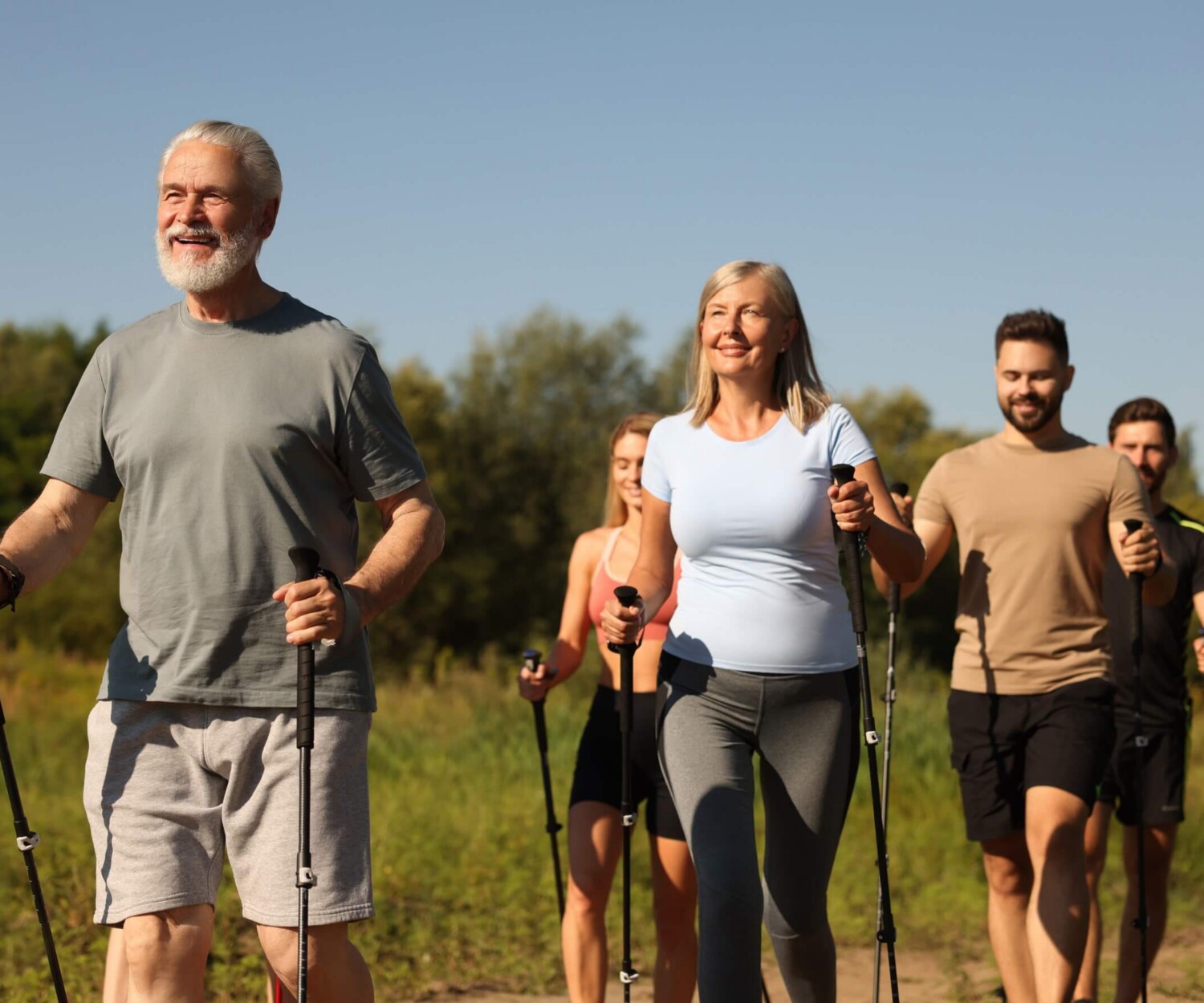 Group of happy people walking with poles outdoors on a sunny day