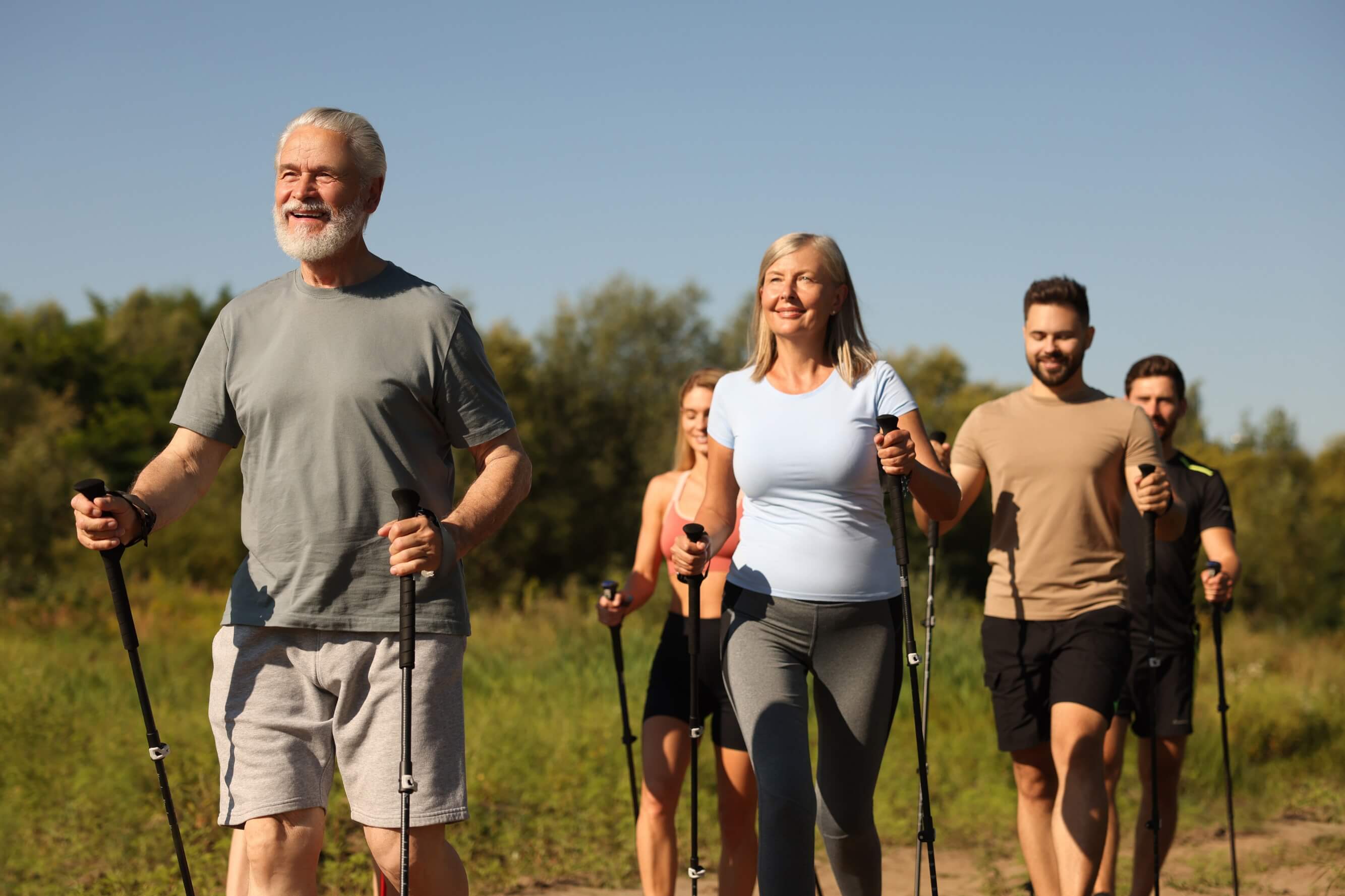 Group of happy people walking with poles outdoors on a sunny day